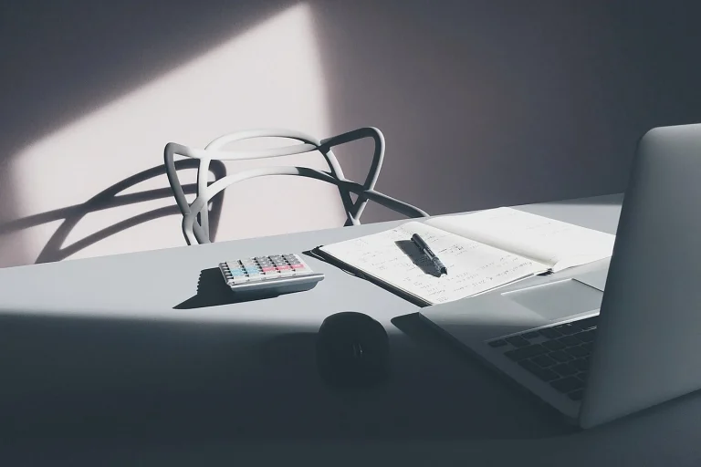 Bureau de travail avec ordinateur, calculatrice et bloc-notes, photographie illustrative.
